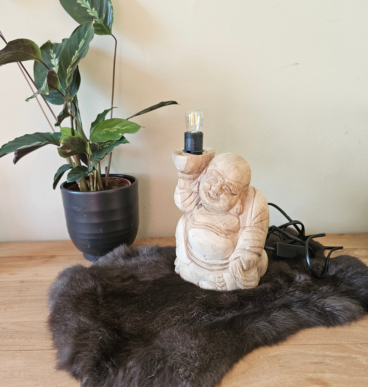 handgemaakt boeddha beeldje van suarhout met ingebouwde verlichting op een kleed naast een plant