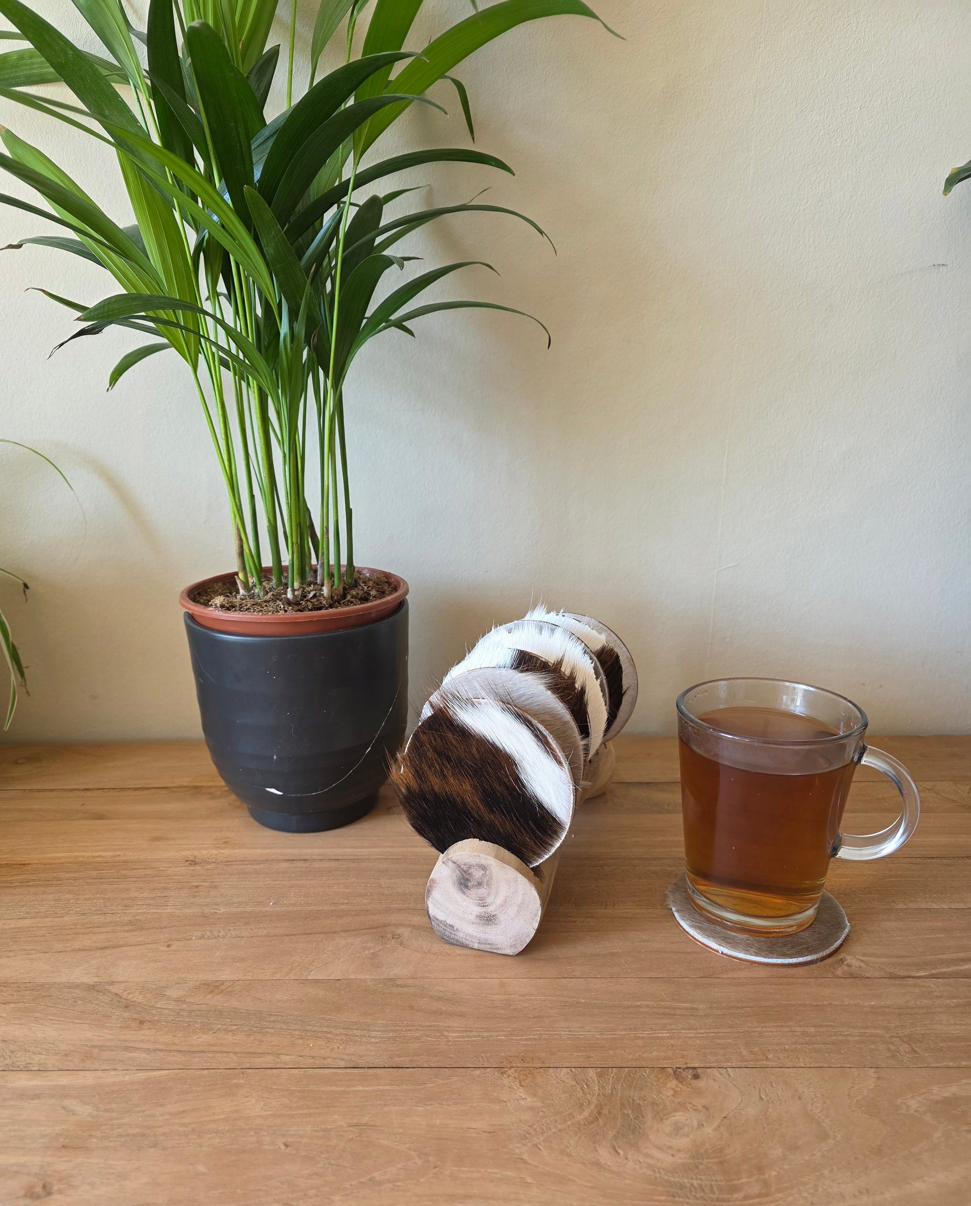 handgemaakte set onderzetters op een standaard naast een glas thee en een plant
