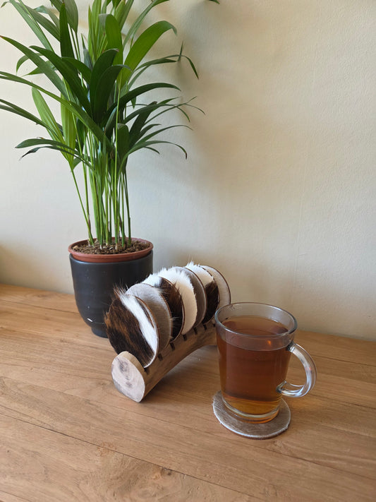 handgemaakte set onderzetters op een standaard naast een glas thee en een plant